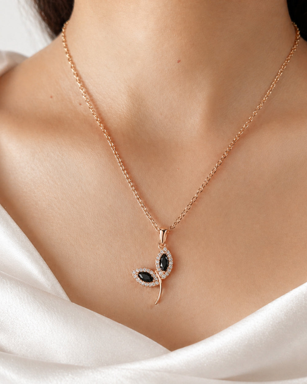 Rose gold necklace with a leaf-shaped pendant on a person wearing a white garment.